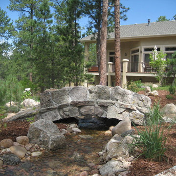 Custom stone bridge over natural design stream and pond