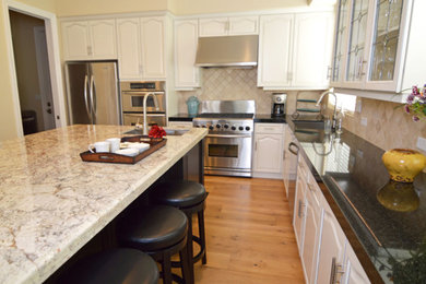 Example of a mid-sized classic l-shaped medium tone wood floor and brown floor open concept kitchen design in Sacramento with a drop-in sink, raised-panel cabinets, white cabinets, granite countertops, beige backsplash, stainless steel appliances, an island and multicolored countertops
