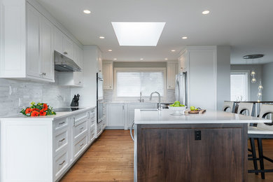 Photo of a large contemporary u-shaped open plan kitchen in Vancouver with a double-bowl sink, recessed-panel cabinets, white cabinets, quartz benchtops, white splashback, stone tile splashback, stainless steel appliances, medium hardwood floors and with island.