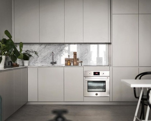 Bild på ett mellanstort nordiskt kök, med släta luckor, grå skåp, marmorbänkskiva, vitt stänkskydd, stänkskydd i marmor, integrerade vitvaror, ljust trägolv och beiget golv