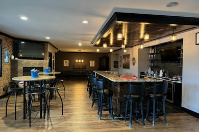Large walk-out laminate floor, multicolored floor, wood ceiling and brick wall basement photo in Detroit with a bar, gray walls, a corner fireplace and a tile fireplace