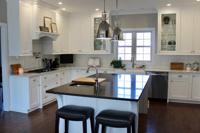 Photo of a large traditional u-shaped eat-in kitchen in St Louis with a farmhouse sink, recessed-panel cabinets, white cabinets, quartz benchtops, white splashback, porcelain splashback, stainless steel appliances, dark hardwood floors, with island and brown floor.
