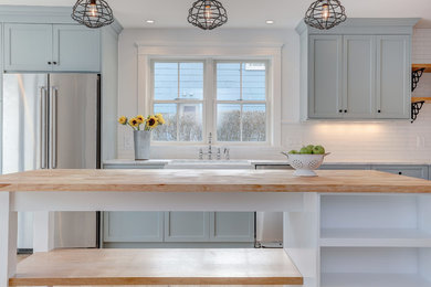 Example of a mid-sized farmhouse galley enclosed kitchen design in New York with a farmhouse sink, shaker cabinets, gray cabinets, wood countertops, white backsplash, subway tile backsplash, stainless steel appliances and an island