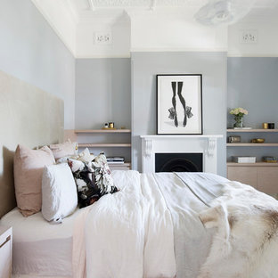 Inredning av ett skandinaviskt mellanstort huvudsovrum, med blå väggar, heltäckningsmatta, en standard öppen spis, en spiselkrans i gips och beiget golv