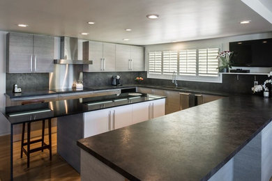 Eat-in kitchen - large contemporary u-shaped medium tone wood floor eat-in kitchen idea in Santa Barbara with stainless steel appliances, an island, an undermount sink, flat-panel cabinets, gray cabinets, black backsplash and stone slab backsplash