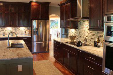 Example of a large transitional l-shaped medium tone wood floor open concept kitchen design in Other with recessed-panel cabinets, dark wood cabinets, granite countertops, multicolored backsplash, glass tile backsplash, stainless steel appliances and an island