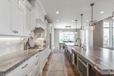 Photo of a large arts and crafts l-shaped eat-in kitchen in Salt Lake City with a farmhouse sink, recessed-panel cabinets, white cabinets, white splashback, brick splashback, stainless steel appliances, light hardwood floors, with island and brown floor.