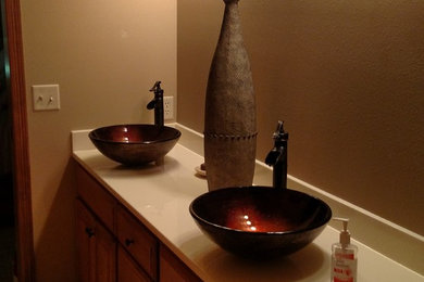Example of a small transitional master ceramic tile and beige floor alcove shower design in Other with raised-panel cabinets, medium tone wood cabinets, a two-piece toilet, brown walls, a vessel sink and solid surface countertops