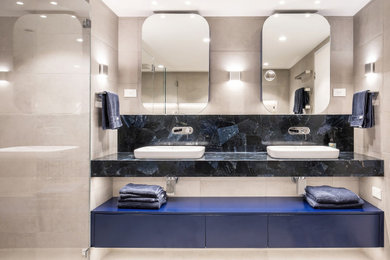 This is an example of a mid-sized contemporary master bathroom in Sydney with flat-panel cabinets, blue cabinets, an alcove shower, a wall-mount toilet, beige tile, porcelain tile, beige walls, porcelain floors, a vessel sink, beige floor, a hinged shower door, blue benchtops, a niche, a double vanity and a floating vanity.