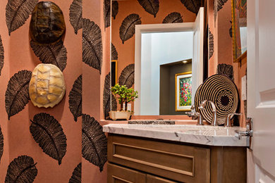 This is an example of a mid-sized eclectic powder room in Phoenix with raised-panel cabinets, medium wood cabinets, multi-coloured walls, light hardwood floors, an undermount sink, marble benchtops, brown floor and white benchtops.
