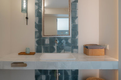 Example of a mid-sized minimalist beige tile and ceramic tile powder room design in New York with recessed-panel cabinets, white cabinets, a wall-mount toilet, a console sink, granite countertops, white countertops and a built-in vanity