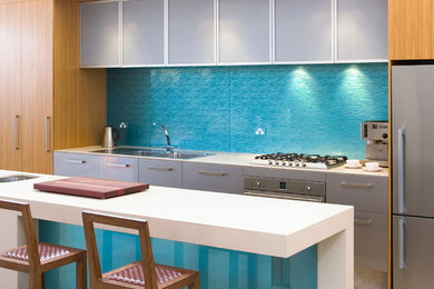 This is an example of a contemporary galley kitchen in Adelaide with glass sheet splashback, flat-panel cabinets, white cabinets, blue splashback, stainless steel appliances and with island.
