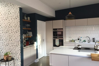 Design ideas for a large modern l-shaped kitchen/diner in Belfast with flat-panel cabinets, beige cabinets, white splashback, ceramic splashback, integrated appliances, concrete flooring, an island, grey floors and white worktops.