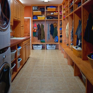他の地域の中サイズのトランジショナルスタイルのおしゃれな家事室 (ドロップインシンク、レイズドパネル扉のキャビネット、人工大理石カウンター、オレンジの壁、磁器タイルの床、上下配置の洗濯機・乾燥機、中間色木目調キャビネット) の写真