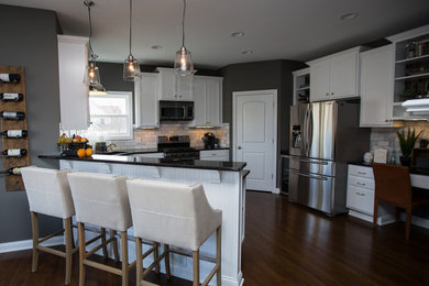 Eat-in kitchen - mid-sized transitional l-shaped medium tone wood floor eat-in kitchen idea in Columbus with an undermount sink, recessed-panel cabinets, white cabinets, solid surface countertops, gray backsplash, ceramic backsplash, stainless steel appliances and an island