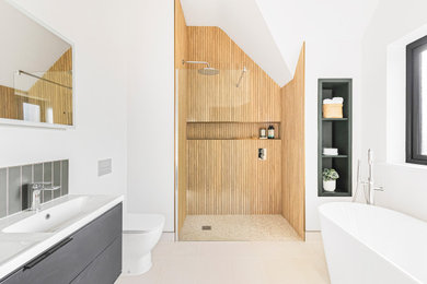 Contemporary ensuite bathroom in Cambridgeshire with flat-panel cabinets, black cabinets, a freestanding bath, a walk-in shower, a built-in sink, an open shower, double sinks, a floating vanity unit, a vaulted ceiling, wood-effect tiles, white walls, porcelain flooring and beige floors.