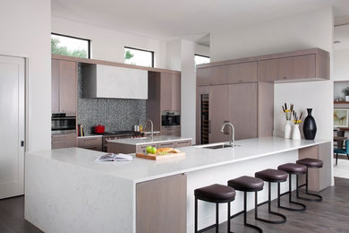 Example of a large minimalist u-shaped light wood floor and brown floor eat-in kitchen design in Raleigh with a drop-in sink, flat-panel cabinets, light wood cabinets, marble countertops, gray backsplash, ceramic backsplash, stainless steel appliances and an island