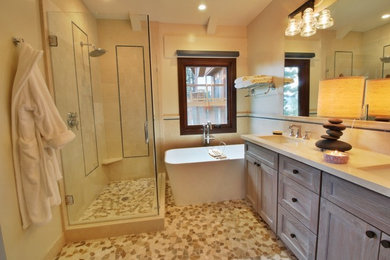 Photo of a mid-sized arts and crafts master bathroom in Sacramento with recessed-panel cabinets, light wood cabinets, a freestanding tub, a corner shower, a two-piece toilet, beige tile, ceramic tile, beige walls, pebble tile floors, an undermount sink, engineered quartz benchtops, multi-coloured floor, a hinged shower door and beige benchtops.