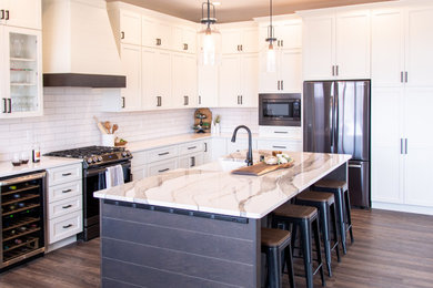 Large transitional l-shaped brown floor eat-in kitchen photo in Other with a farmhouse sink, shaker cabinets, white cabinets, quartz countertops, white backsplash, ceramic backsplash, an island and white countertops