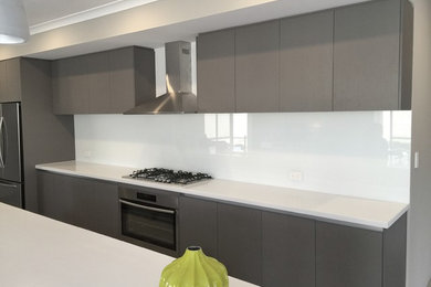 Design ideas for a mid-sized modern galley eat-in kitchen in Perth with a triple-bowl sink, raised-panel cabinets, medium wood cabinets, quartz benchtops, white splashback, glass sheet splashback, stainless steel appliances and with island.