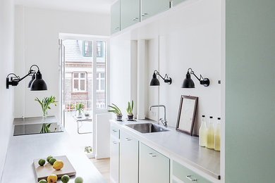 Inspiration for a scandinavian galley separate kitchen in Copenhagen with an integrated sink, flat-panel cabinets, green cabinets, concrete benchtops, grey splashback, light hardwood floors, no island and beige floor.