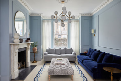 Photo of a traditional living room in London with blue walls, light hardwood floors, a standard fireplace and beige floor.