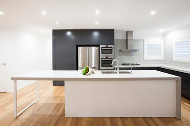 Inspiration for a mid-sized contemporary l-shaped eat-in kitchen with an undermount sink, flat-panel cabinets, solid surface benchtops, grey splashback, glass sheet splashback, stainless steel appliances, medium hardwood floors, with island, brown floor and blue cabinets.