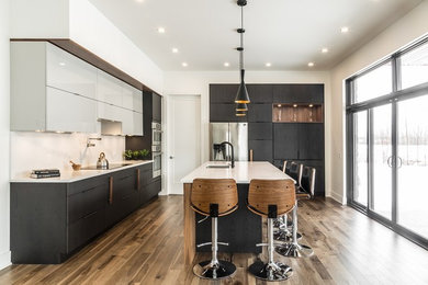 Example of a large trendy l-shaped medium tone wood floor kitchen design in Montreal with an undermount sink, flat-panel cabinets, dark wood cabinets, quartz countertops, white backsplash, stainless steel appliances and an island