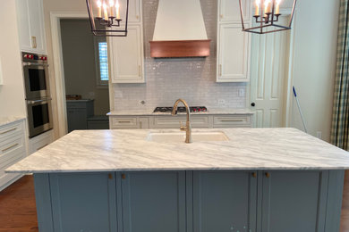 Mid-sized elegant l-shaped medium tone wood floor, brown floor and coffered ceiling open concept kitchen photo in Atlanta with an undermount sink, beaded inset cabinets, white cabinets, marble countertops, white backsplash, terra-cotta backsplash, stainless steel appliances, an island and white countertops