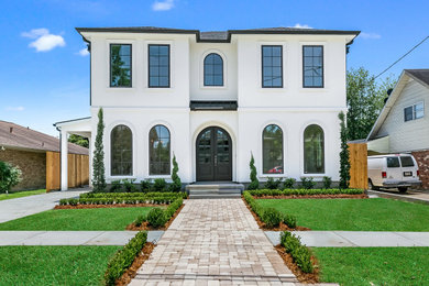 Large transitional white two-story stucco exterior home idea in New Orleans with a shingle roof and a brown roof