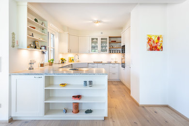 Kleine Landhausstil Küche ohne Insel mit Landhausspüle, Kassettenfronten, weißen Schränken, Granit-Arbeitsplatte, schwarzen Elektrogeräten, braunem Holzboden, braunem Boden und grauer Arbeitsplatte in München
