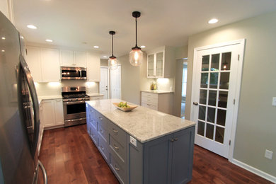 Mid-sized transitional l-shaped medium tone wood floor and brown floor enclosed kitchen photo in Minneapolis with shaker cabinets, white cabinets, granite countertops, white backsplash, stainless steel appliances, an island and white countertops
