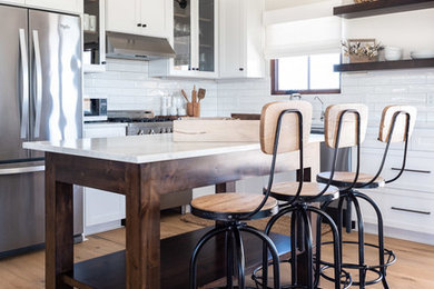 This is an example of a mid-sized country l-shaped open plan kitchen in San Luis Obispo with a farmhouse sink, shaker cabinets, white cabinets, marble benchtops, white splashback, subway tile splashback, stainless steel appliances, light hardwood floors, with island, brown floor and white benchtop.
