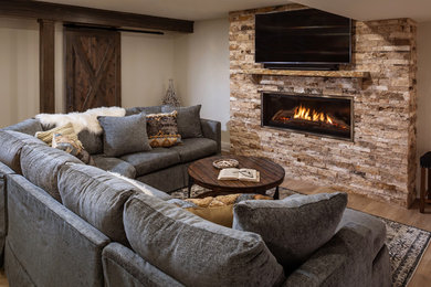Photo of a mid-sized beach style walk-out basement in Milwaukee with beige walls, vinyl floors, a standard fireplace, a stone fireplace surround and brown floor.