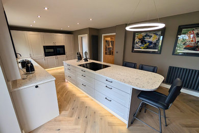 Design ideas for a large modern l-shaped kitchen/diner in West Midlands with a submerged sink, shaker cabinets, beige cabinets, quartz worktops, white splashback, engineered quartz splashback, black appliances, laminate floors, an island, brown floors and white worktops.