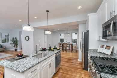 Inspiration for a mid-sized transitional single-wall medium tone wood floor and brown floor open concept kitchen remodel in Baltimore with an undermount sink, raised-panel cabinets, white cabinets, granite countertops, white backsplash, subway tile backsplash, stainless steel appliances, an island and gray countertops