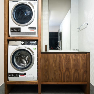 This is an example of a small contemporary single-wall separated utility room in Madrid with an integrated sink, open cabinets, medium wood cabinets, engineered stone countertops, white walls, slate flooring, a stacked washer and dryer, grey floors and black worktops.