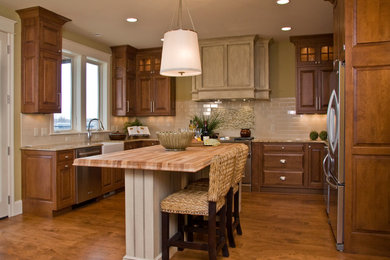 Mid-sized traditional u-shaped eat-in kitchen in Grand Rapids with a farmhouse sink, raised-panel cabinets, medium wood cabinets, granite benchtops, white splashback, subway tile splashback, stainless steel appliances, bamboo floors and with island.