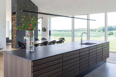 This is an example of a large scandinavian galley open plan kitchen in Aarhus with a single-bowl sink, dark wood cabinets, with island and grey benchtop.