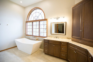 Photo of a mid-sized transitional master bathroom in Chicago with flat-panel cabinets, a freestanding tub, porcelain tile, porcelain floors, an undermount sink, granite benchtops, a hinged shower door, medium wood cabinets, an alcove shower, a two-piece toilet, beige tile, beige walls and beige floor.