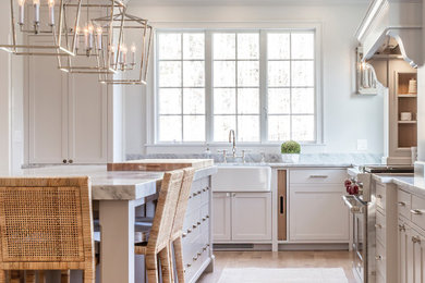 Inspiration for a large traditional u-shaped open plan kitchen in Boston with a farmhouse sink, light hardwood floors, with island and white benchtop.