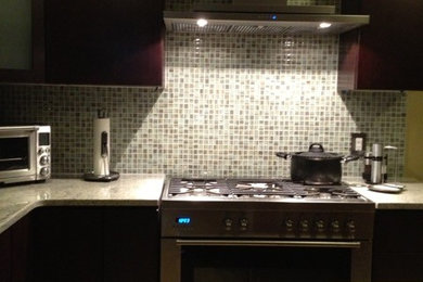 Inspiration for a porcelain tile kitchen remodel in New York with a farmhouse sink, flat-panel cabinets, dark wood cabinets, granite countertops, multicolored backsplash, glass tile backsplash, stainless steel appliances and an island