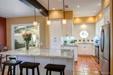 Inspiration for a mid-sized mediterranean u-shaped open plan kitchen in San Diego with an undermount sink, shaker cabinets, white cabinets, granite benchtops, white splashback, glass tile splashback, stainless steel appliances, terra-cotta floors and with island.