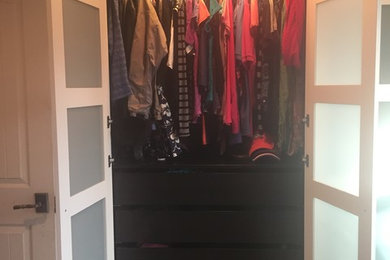 Inspiration for a small modern gender-neutral carpeted reach-in closet remodel in Denver with glass-front cabinets and white cabinets