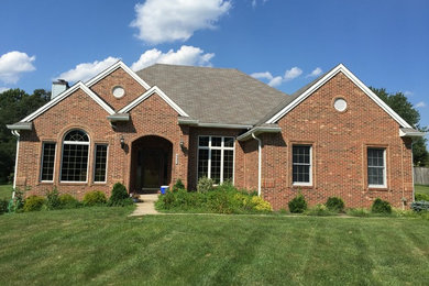 Example of a large classic red one-story brick house exterior design in Baltimore with a clipped gable roof and a shingle roof