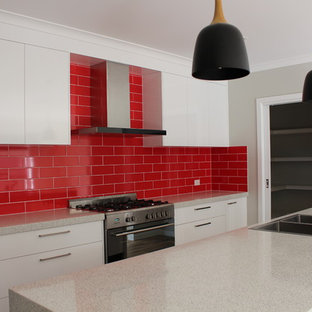 Idées déco pour une arrière-cuisine parallèle contemporaine de taille moyenne avec un évier posé, un placard à porte plane, des portes de placard blanches, un plan de travail en quartz modifié, une crédence rouge, une crédence en carrelage métro, un électroménager en acier inoxydable, un îlot central et un plan de travail blanc.