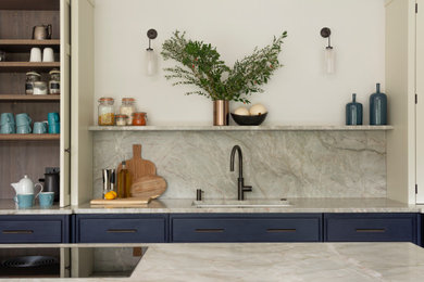Photo of a large contemporary u-shaped open plan kitchen in Berkshire with a built-in sink, beaded cabinets, blue cabinets, marble worktops, green splashback, marble splashback, integrated appliances, limestone flooring, an island, beige floors, green worktops and feature lighting.