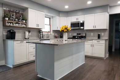 Mid-sized country u-shaped eat-in kitchen in Cleveland with an undermount sink, shaker cabinets, white cabinets, granite benchtops, white splashback, subway tile splashback, stainless steel appliances, laminate floors, with island, brown floor and grey benchtop.