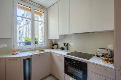 Aménagement d'une petite cuisine classique en L fermée avec un évier encastré, un placard à porte affleurante, des portes de placard rose, un plan de travail en surface solide, une crédence blanche, une crédence en céramique, un électroménager noir, tomettes au sol, un sol beige et un plan de travail blanc.