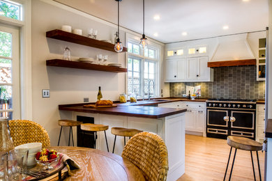 Mid-sized traditional u-shaped eat-in kitchen in San Francisco with a single-bowl sink, shaker cabinets, white cabinets, wood benchtops, grey splashback, ceramic splashback, stainless steel appliances, light hardwood floors, a peninsula and beige floor.